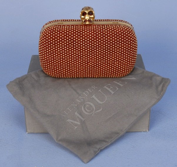 DEADSTOCK ALEXANDER McQUEEN SKULL CLASP CLUTCH.: Burgundy velvet having hinged brass frame with push back clasp in the form of a skull set with faceted red stones, removable leather shoulder strap with hidden hinge mounts and leather interior, with 