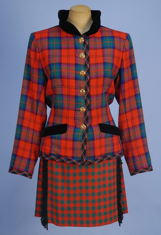 YVES SAINT LAURENT RIVE GAUCHE SKIRT SUIT, LATE 20th C.: Red and green plaid jacket having black velvet collar, angled pockets and back panel with tie, colorful braided trim and enameled buttons. Wrap skirt in smaller scale plaid with side pleats, trimmed i
