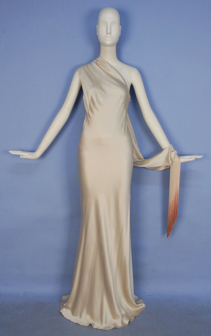 ALEXANDER McQUEEN ASYMMETRICAL SATIN EVENING GOWN.: Oyster sheath in silk-acetate blend having one shoulder draped across back into a deep cuff with self buttons and long ombreed fringe, slightly flared at hem. Labeled. Marked size 42. Excellent.