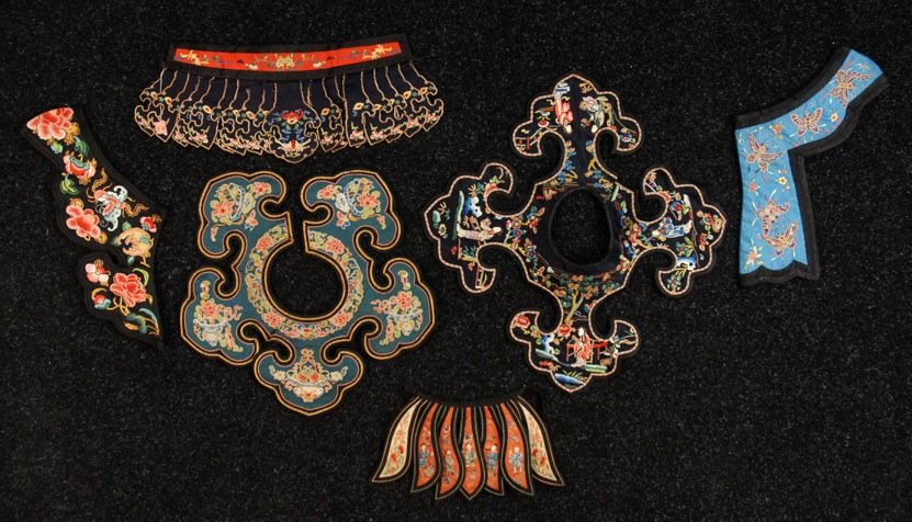 FOUR CHINESE COLLARS, 19th - 20th C.: All dark silk worked in satin and Peking stitch, some with couched gold thread. Together with two long flap headbands. Largest 14 inches in diameter. Excellent.