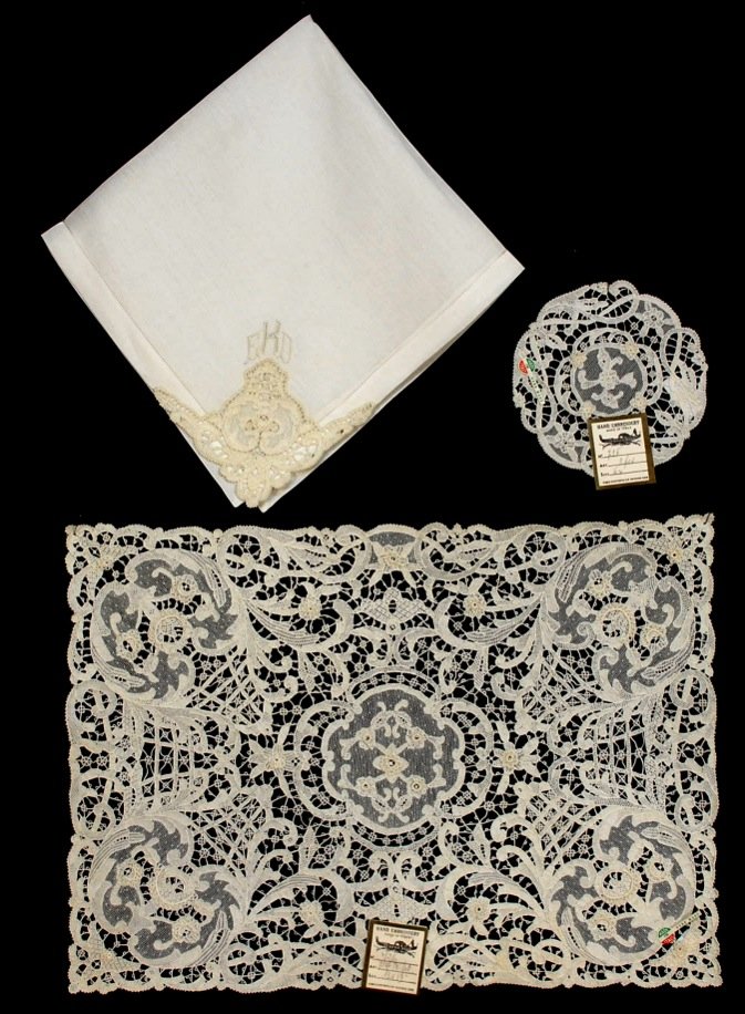 DEADSTOCK HANDMADE ITALIAN NEEDLE LACE TABLE LINEN SET,: White linen consisting of twelve each: Allover lace placemats, 18 1/2 x 13 1/2, napkins with lace corner and EDK monogram, 20 1/2 x 20 1/4, and lace goblet rounds, 5 1/2 diameter. Excellent. IMA.