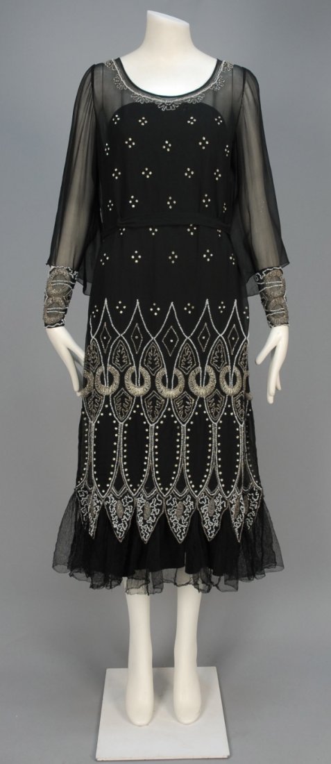 BEADED CHIFFON DINNER DRESS, 1920s.: Black silk having an Arabesque pattern of crystal and milk glass beads with prong set rhinestones, long flared sleeve with beaded narrow cuff, Van Dyke pointed hem over tulle ruffle, self belt. B-38, 