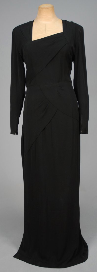 GILBERT ADRIAN CREPE DINNER DRESS, 1940s.: Black with long, zippered sleeve, padded shoulder, asymmetrical drape on bodice front and around one hip, continuing into a floating swag around skirt back joined at the opposite side just below knee.