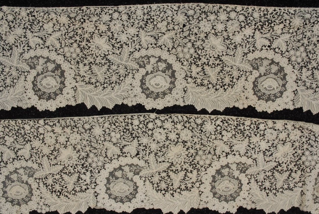 BRUSSELS MIXED LACE TRIM, EARLY 20th C.: Pair of long tapering duchesse panels with repeating inset of needle lace rose on net. Widest 11 inches, each 108 inches long. (Broken brides, mostly along scalloped edge, small stain) good.