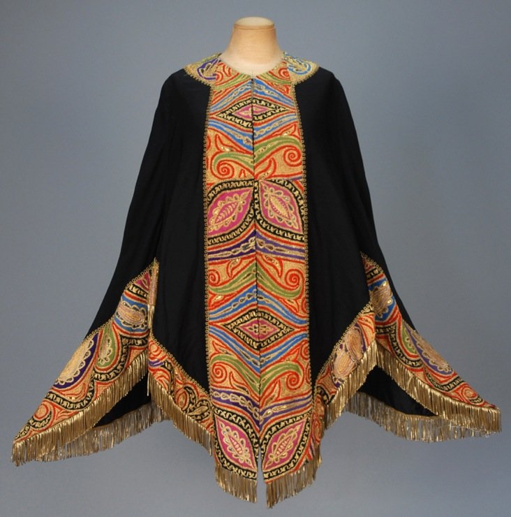 FARMER & ROGERS WOOL CAPE with METALLIC EMBROIDERY, c.: Black with polychrome wool trim in a stylized paisley heavily embroidered with metallic gold thread and decorated with sequins, metallic fringe and long cord tassels at back, quilted silk lining. Labe