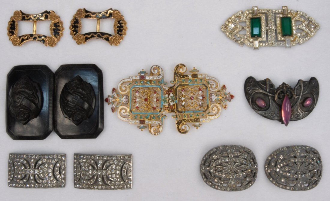 SEVEN BUCKLES, 1915 - 1930s.: Four belt buckles: One gilt filigree with enamel decoration, one having paste and emerald cut green glass stones, one gutta percha with belted floral relief, one white metal Art Nouveau design set wit