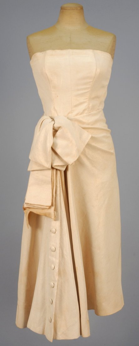 JACQUES FATH for JOSEPH HALPERT STRAPLESS SUMMER DRESS,: Corded ivory silk and metallic gold stripe having boned bodice, full skirt with front self buttons below five large tucks incorporating a large self bow off center at waist. Labeled. B-32, W-24, L-41.