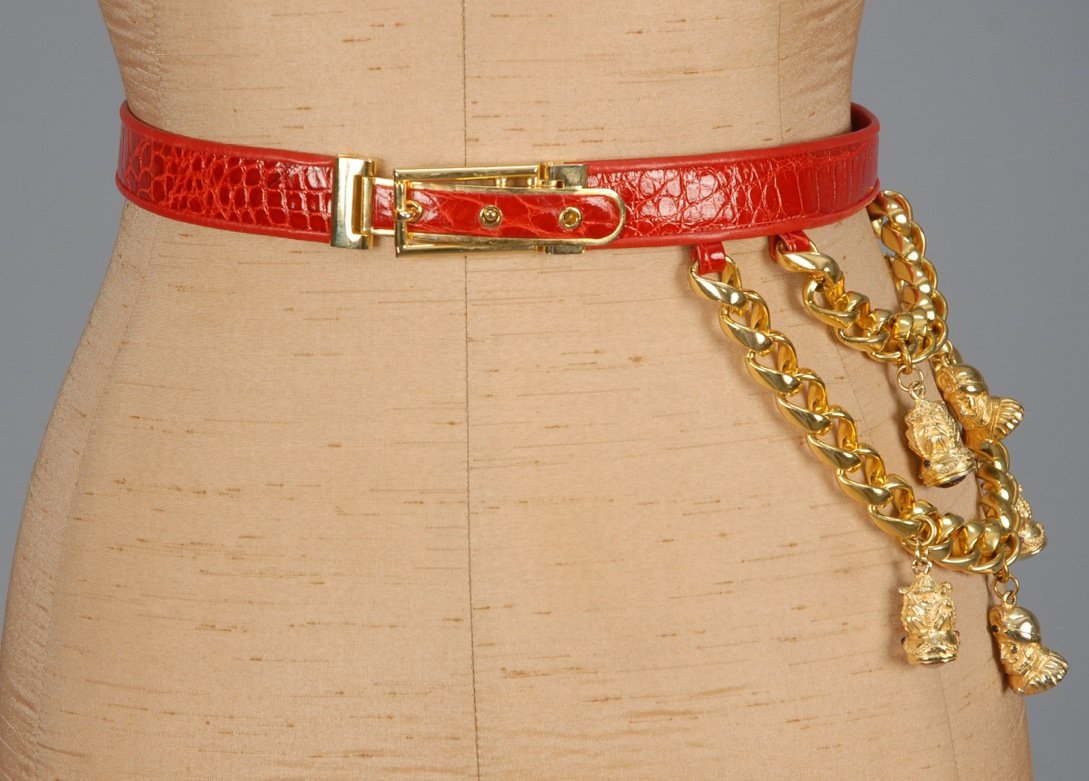 JUDITH LEIBER NOVELTY BELT.: Adjustable red reptile embossed leather belt with gold tone buckle and double swag of heavy links to one side adorned with five figural charms set with semi precious stones. Labeled. 1 inch wide, fits