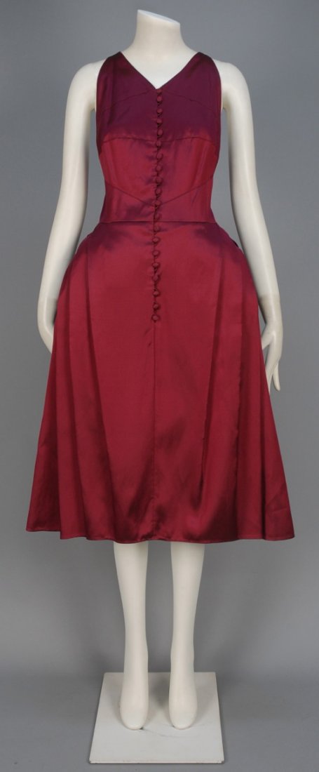 KARL LAGERFELD SILK COCKTAIL DRESS.: Sleeveless plum fitted bodice having low back with crossed straps and self buttons, full skirt padded at hip with crossed side pleats. Labeled. B-36, W-28, L-44. Excellent.