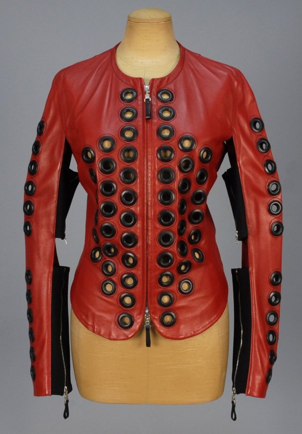 GIANFRANCO FERRE LEATHER JACKET with GROMMETS.: Cinnabar lambskin having open seam to the undersleeve joined with two black elastic zippered panels, front and sleeve decorated with large black leather grommets and topstitching, front zipper. Labele