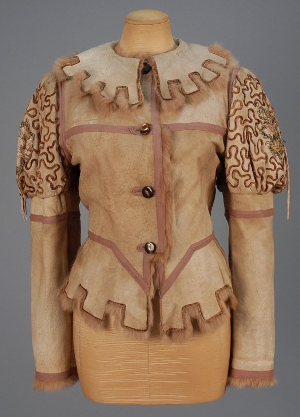 MEDIEVAL STYLE SHEARLING JACKET.: Natural color hide with crenelated collar and peplum having mauve trim bands and rabbit lining, puffed upper sleeve decorated in chenille and floral applique with metallic threads and tassels. Italian