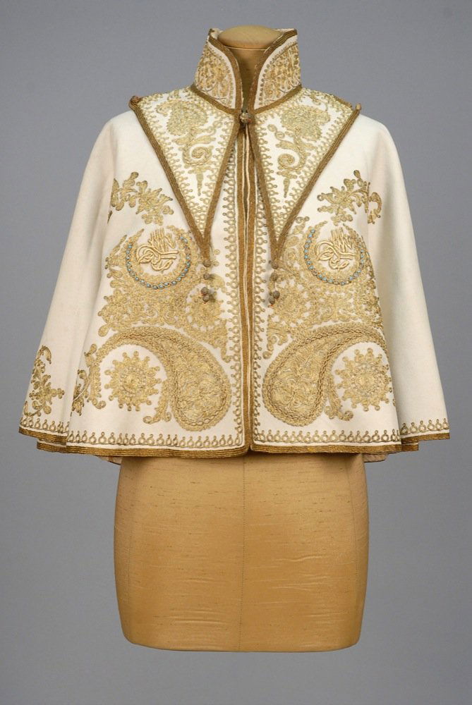 TWO-PIECE METALLIC EMBROIDERED CAPELET, EARLY 20th C.: TWO-PIECE METALLIC EMBROIDERED CAPELET, EARLY 20th C. Cream felt with couched gold cord decoration of scrolls and botehs having satin stitch Persian script within two crescents set with turquoise ston