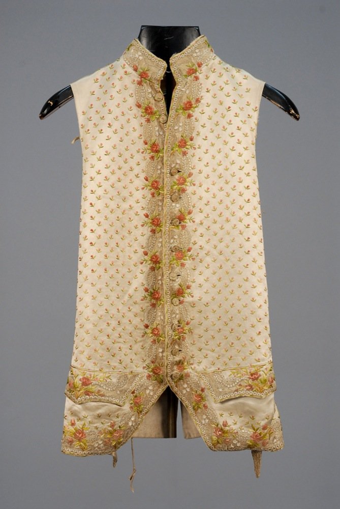 GENTS SILK EMBROIDERED WAISTCOAT with LACE TRIM, 1750 -: GENTS SILK EMBROIDERED WAISTCOAT with LACE TRIM, 1750 - 1775. Cream satin with stand collar, shaped pocket flap and border appliqued with ecru net embroidered in ecru, pink and green satin stitch flor
