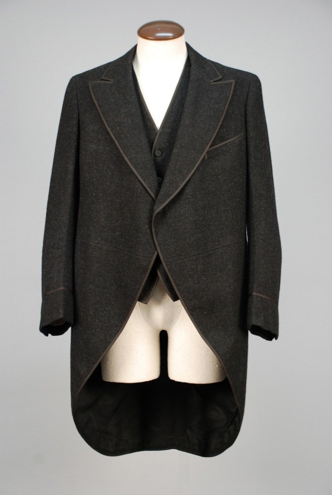 GENTS CUTAWAY WOOL COAT and VEST, EARLY 20th C. Black: GENTS CUTAWAY WOOL COAT and VEST, EARLY 20th C. Black twill weave with flecks of charcoal grey, coat having extended lapel, single basketweave button and braided bindings, silk twill lining. Matching 