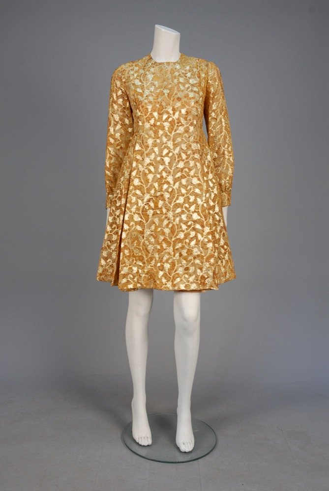 METALLIC BROCADE COCKTAIL DRESS, 1960s. Pale gold: METALLIC BROCADE COCKTAIL DRESS, 1960s. Pale gold chiffon printed with ribbon floral in shades of brown, having metallic brocade vines, long cuffed sleeve, A-line skirt with inverted pleats, crepe und