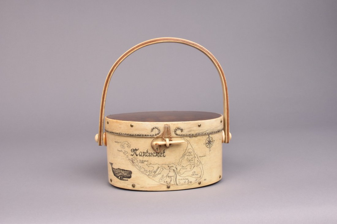 NANTUCKET SCRIMSHAW DITTY BOX, c. 1970: Hinged lid oval box crafted antique bone fingerlap and rosewood construction, bone and wood bent bail handle, depicting map of Nantucket with whale and compass, nailhead trim, bone ring and peg with c