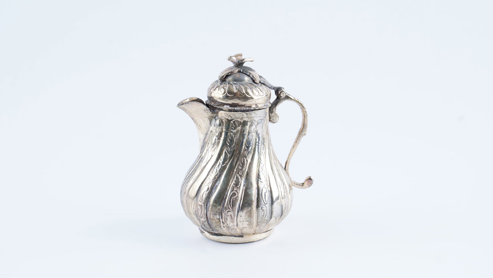 AN OTTOMAN OR ORIENTAL SILVER-PLATED MINIATURE COFFEE POT, LATE 19TH / EARLY 20TH CENTURY: A finely crafted miniature coffee pot of elegant baluster form, featuring a hinged lid and a scrolled handle. The body is richly decorated with repoussé and chased floral scrolls within vertically lo