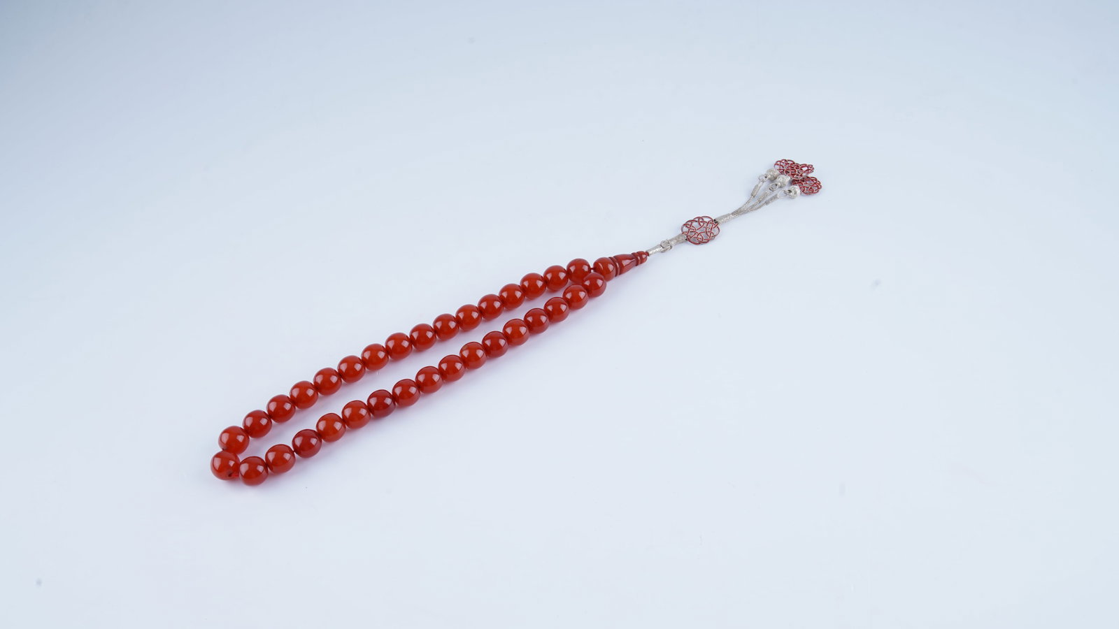 A STRAND OF OLD CHERRY AMBER (FATURAN) PRAYER BEADS (TESBIH), EARLY 20TH CENTURY: A finely presented strand of prayer beads (tesbih), offered as Old Cherry Amber (Faturan Bakelite), dating to the early 20th century. The beads display a warm translucent cherry-red coloration, charac