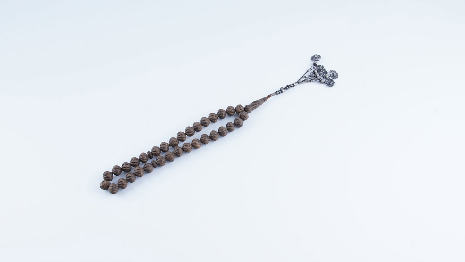 AN OTTOMAN-STYLE MISK-I AMBER PRAYER BEADS WITH KAZAZ SILVER TASSEL: A rare and visually striking strand of prayer beads (tesbih), offered as Misk-i Amber, measuring approximately 19 in (48.3 cm) in length. The beads are of large scale and carved in a traditional form,