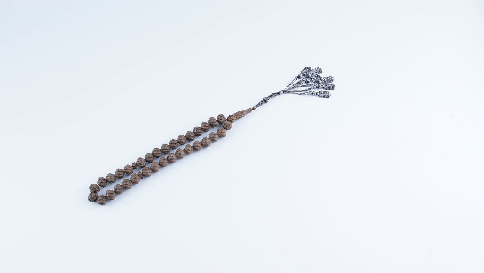 AN OTTOMAN-STYLE MISK-I AMBER PRAYER BEADS WITH KAZAZ SILVER TASSEL: A rare and visually striking strand of prayer beads (tesbih), offered as Misk-i Amber, measuring approximately 18 in (45.7 cm) in length. The beads are of large size and carved in a traditional form, 
