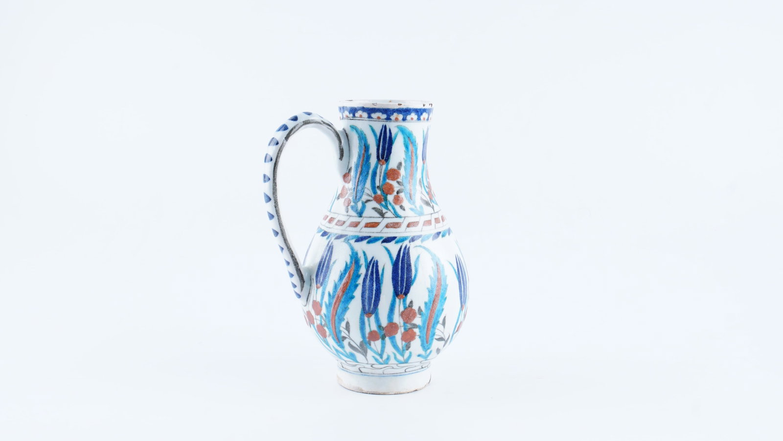AN OTTOMAN IZNIK POLYCHROME POTTERY JUG, EARLY 17TH CENTURY (CIRCA 1600–1620): A fine Ottoman Iznik polychrome pottery jug, dating to the early 17th century (circa 1600–1620), reflecting the established decorative tradition of Iznik ceramic production. Potted in white fritware