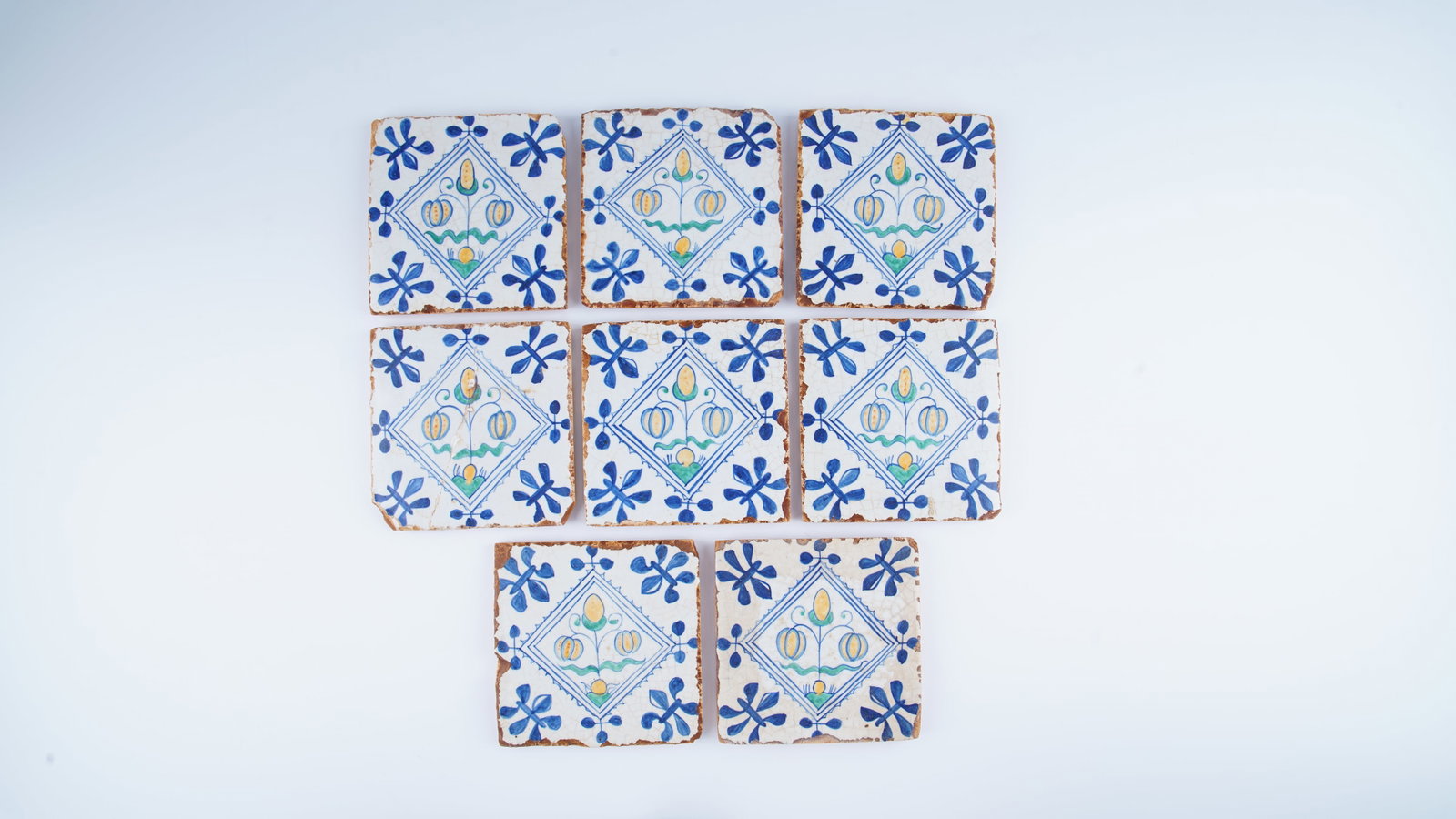 FINE SET OF EIGHT EUROPEAN POLYCHROME TILES IN THE DELFT MANNER, 18TH CENTURY: A fine set of eight polychrome pottery tiles decorated in the Delft manner, each centered with a diamond-shaped panel enclosing a stylized floral composition. Executed in cobalt blue, yellow, and gree