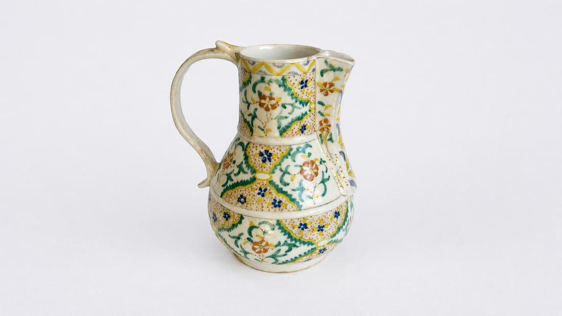 AN OTTOMAN KUTAHYA POLYCHROME POTTERY EWER LATE 18TH – EARLY 19TH CENTURY: An Ottoman Kütahya polychrome pottery ewer, executed in underglaze decoration on a white ceramic body, dating to the late 18th to early 19th century. The surface is richly adorned with stylized flora