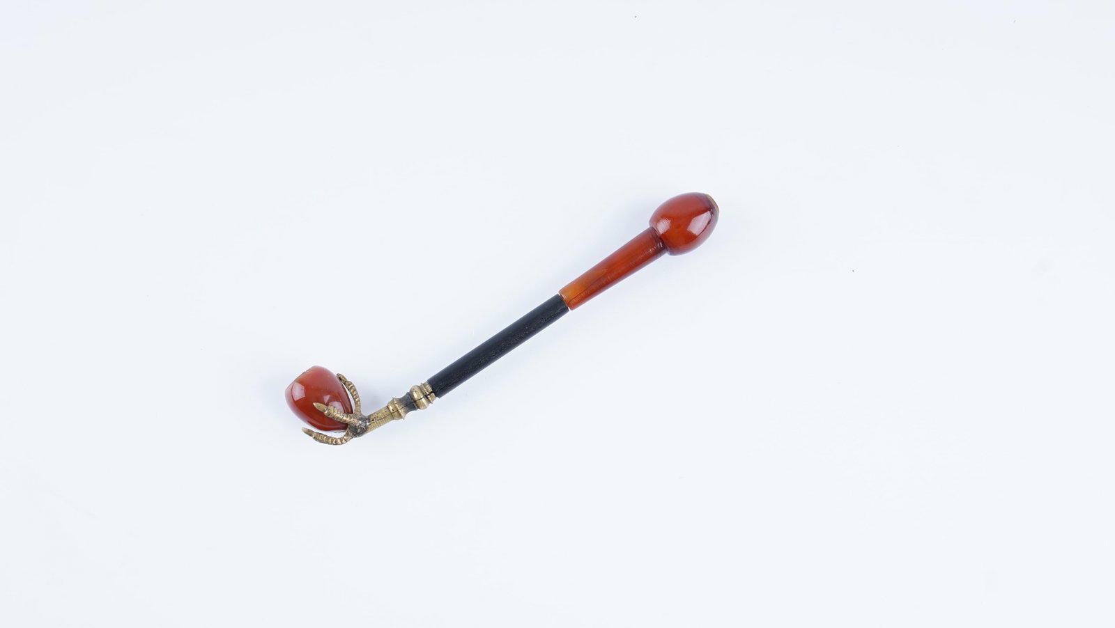 ANTIQUE SMOKING PIPE MOUTHPIECE WITH CARNELIAN-COLORED STONE FINIAL AND CHERRY AMBER (FATURAN): An antique smoking pipe mouthpiece dating to the early 20th century, composed of a refined combination of materials. The piece features a polished carnelian-colored stone finial set within a decorativ