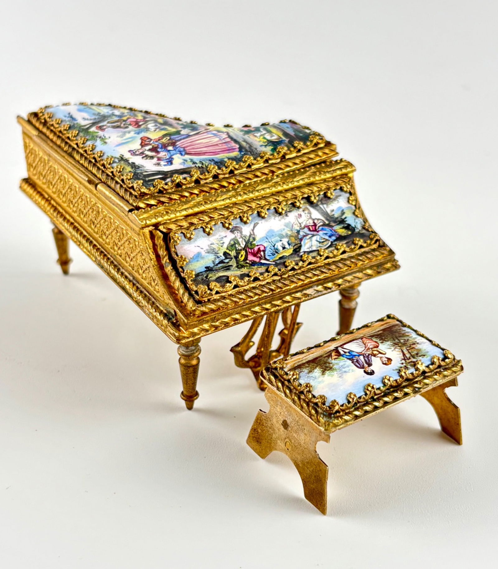 Viennese Miniature Enamel Grand Piano with Bench, Late 19th Century: Miniature Viennese grand piano and matching bench crafted in gilt bronze with detailed enamel panels. The piano and bench feature hand-painted pastoral scenes and gilt floral embossing. Hinged lid ope