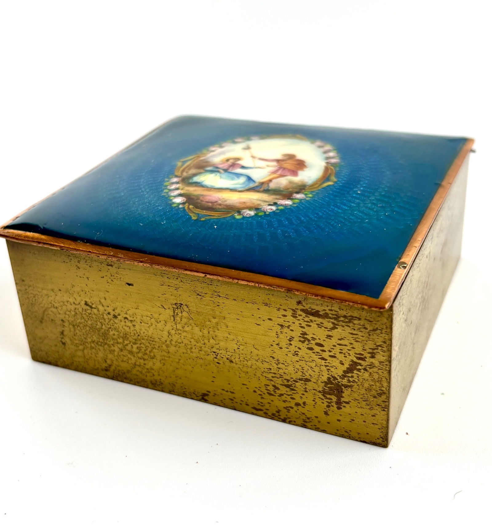 Antique Guilloche Enamel and Gilt Tobacco Box (Austria): A gilt metal tobacco box featuring an intricately detailed guilloche enamel lid with a central figural scene depicting a man and woman in a pastoral setting, surrounded by a floral border. The box sho