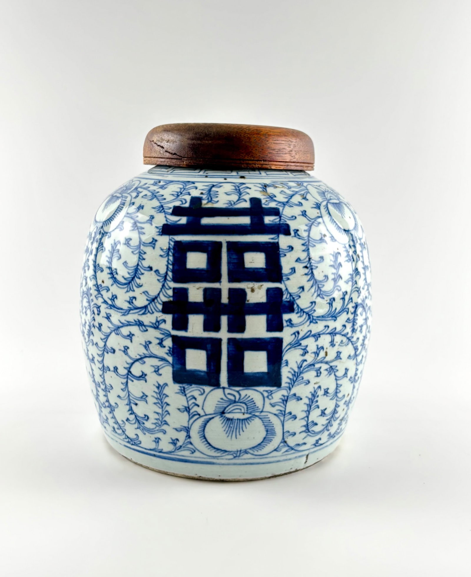 Late Qing Dynasty Blue and White Ginger Jar with Wooden Lid: Blue and white porcelain ginger jar from the late Qing dynasty featuring intricate floral and geometric patterns, including prominent double happiness symbols on its sides. The jar has a smooth glaze 