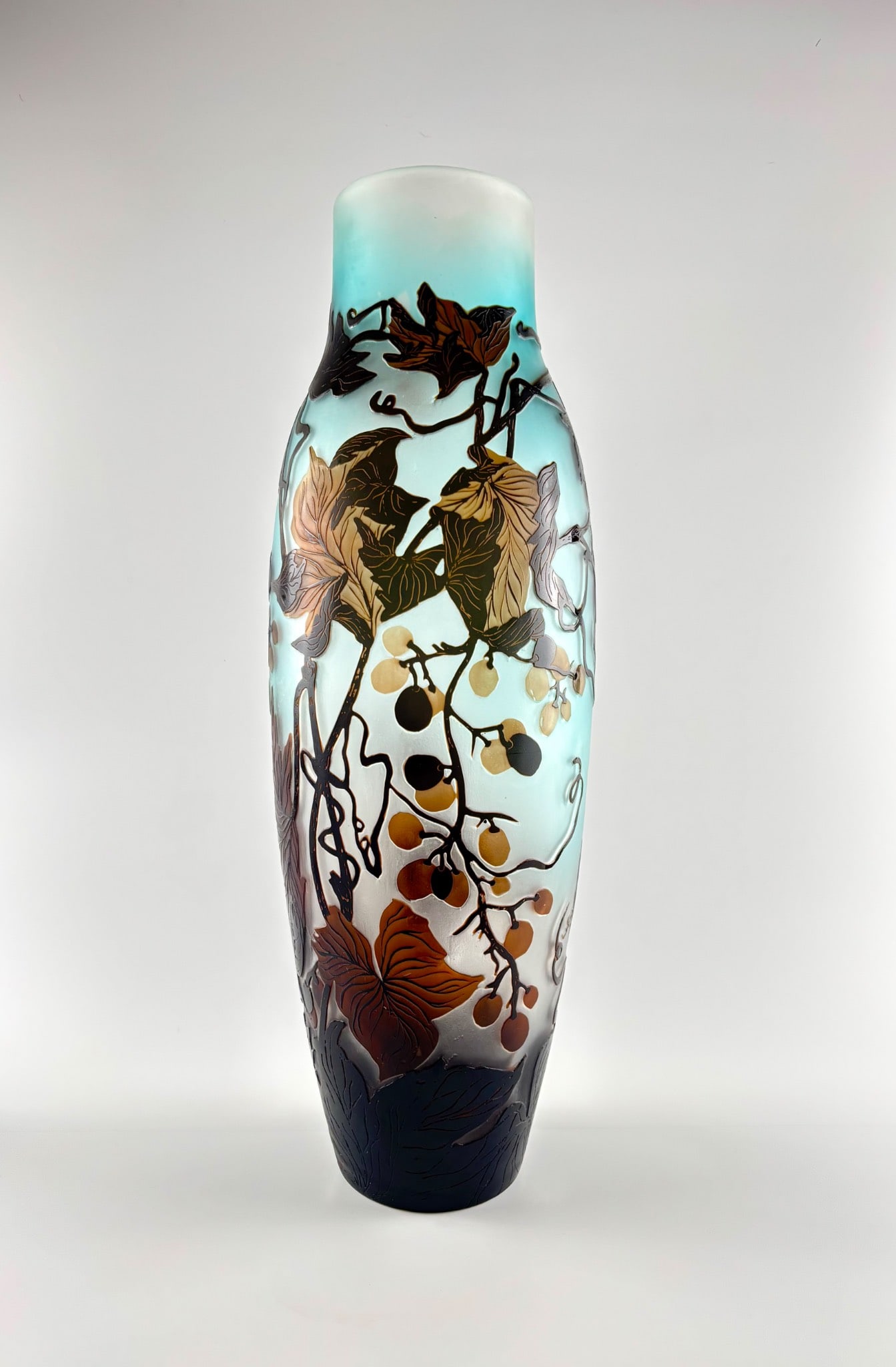 Emile Gallé Acid Etched Cameo Glass Vase with Vine Motif: A tall, vari-colored cameo glass vase in the style of Émile Gallé, featuring an applied intricate vine and leaf motif in brown and golden tones against a frosted blue background. The vase is
