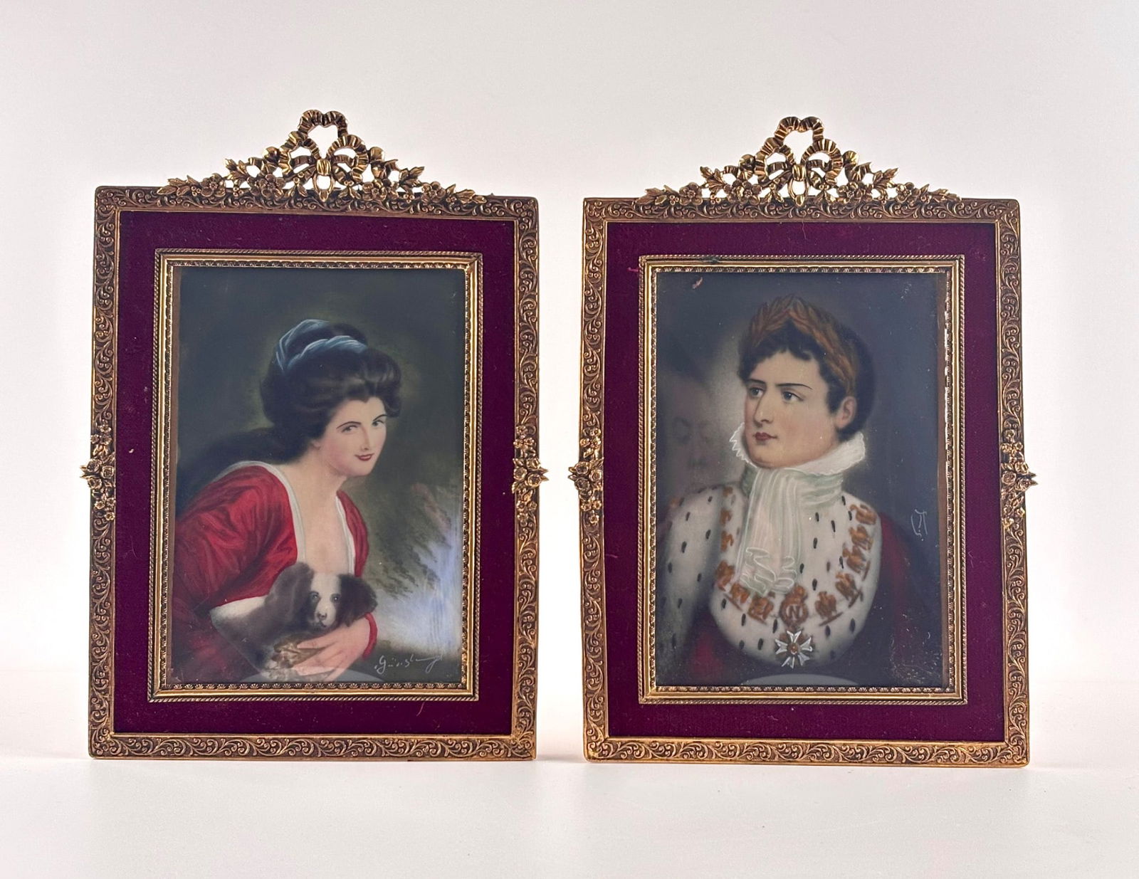 Hand-Painted Portrait Miniatures in Gilt Frames with Velvet Trim: Rectangular portrait miniatures, one depicting a woman in a red dress holding a small dog, the other showing a figure adorned in robes with medals. Both portraits are signed. Both are enclosed i
