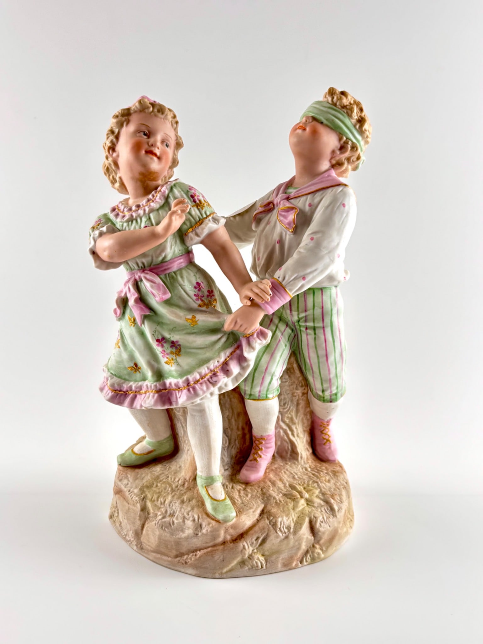 Gebrüder Heubach German Porcelain Figurine, Turn of the Century: A Gebrüder Heubach German porcelain figurine depicting two children playing, crafted around the turn of the century. Features hand-painted details, including floral patterns and pastel tones. The
