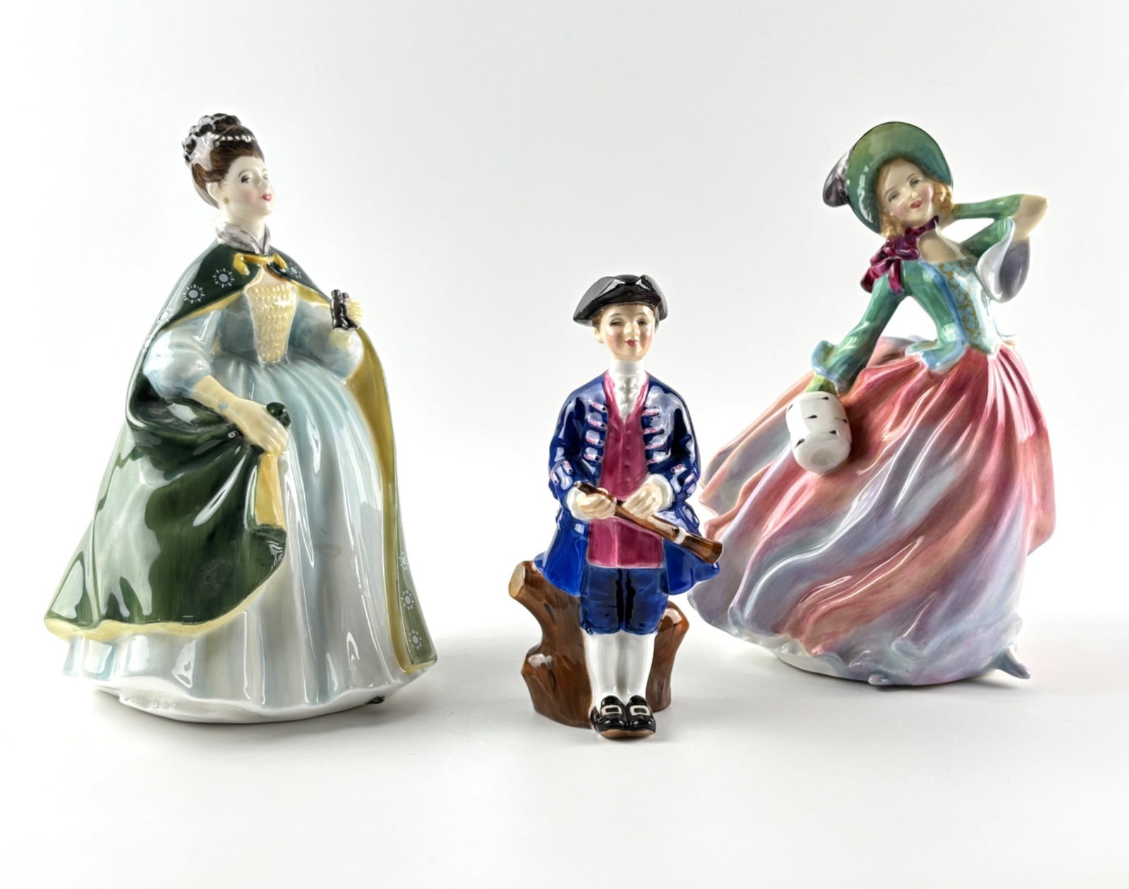Three Royal Doulton Figurines: Three hand-painted bone china figurines by Royal Doulton. Includes ‘Première’ (HN 2343, yellow, green, and blue palette, slight wear), ‘Autumn Breezes’ (HN 1911, pink and green palette, base