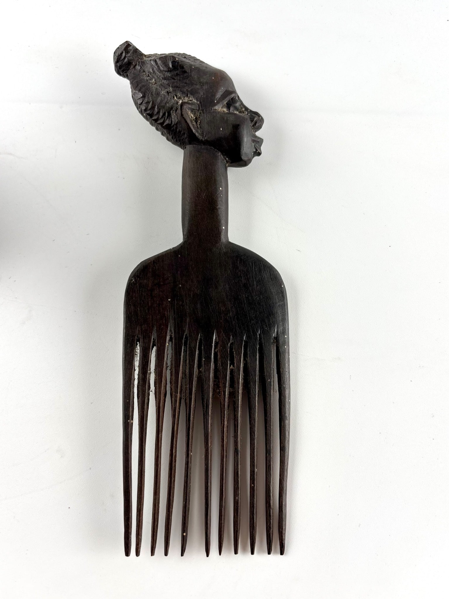 African Hand-Carved Wooden Comb with Female Head Design: Hand-carved wooden comb featuring a sculptural depiction of a female head with detailed facial features and braided hair. The comb has a slender shaft that transitions into finely carved teeth. Eviden