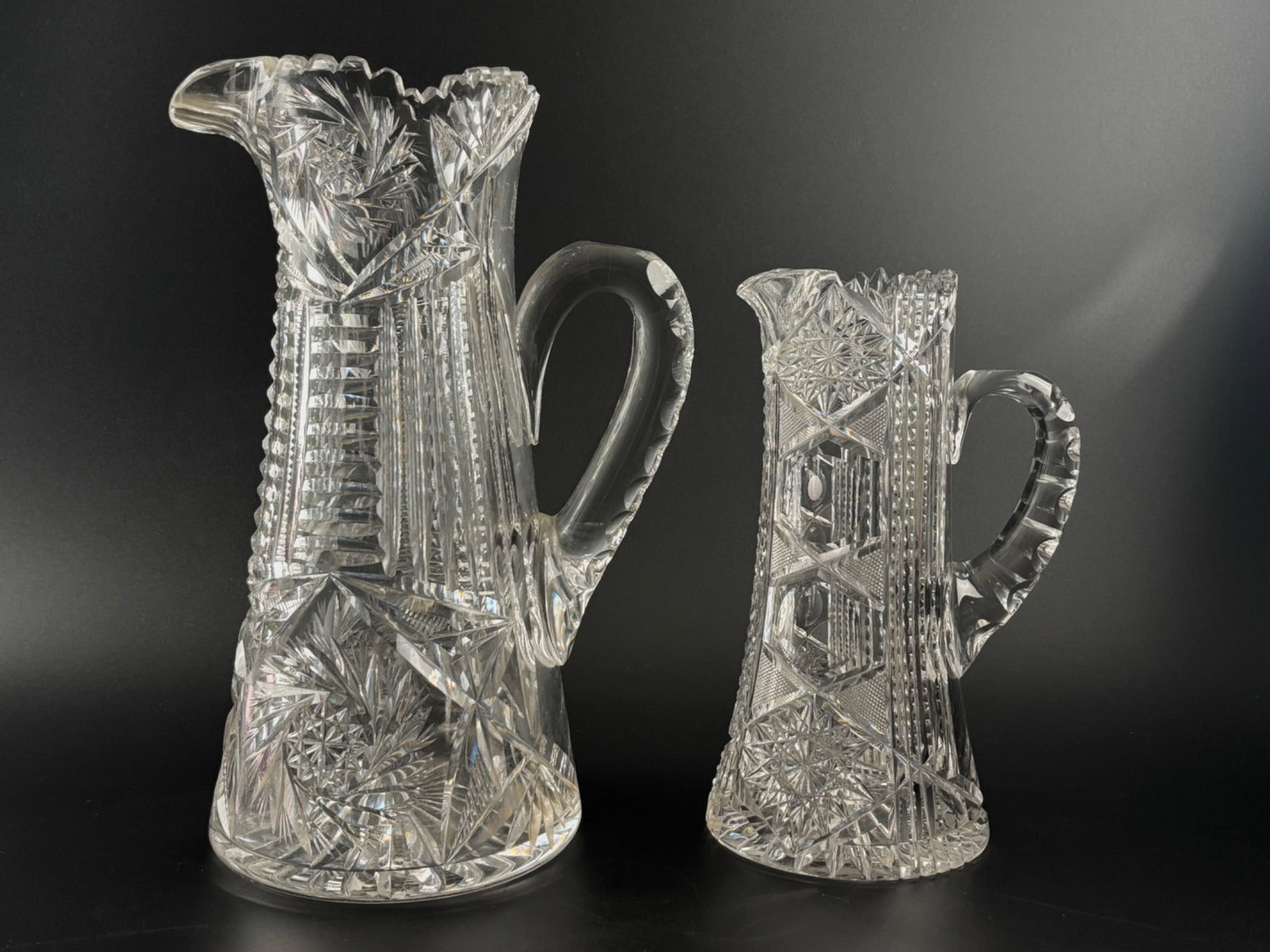 American Brilliant Period Cut Glass Pitchers: American Brilliant Period cut glass pitchers, showcasing intricate geometric and floral patterns characteristic of the era. Each pitcher features precision-cut designs including hobstars, fans, and pa