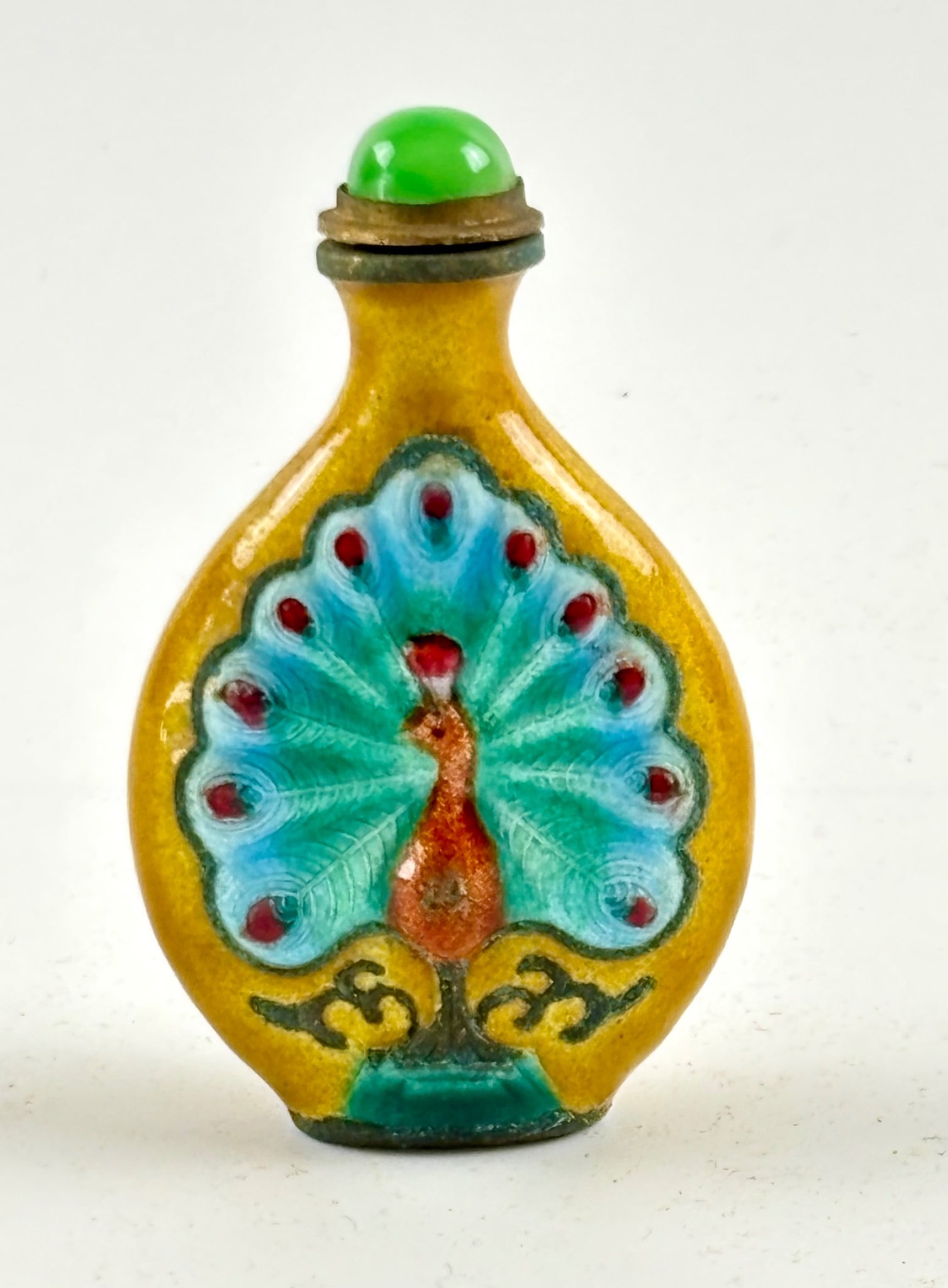 Enameled Glass Snuff Bottle with Peacock Motif: Flattened ovoid glass snuff bottle featuring a peacock motif in raised enamel detailing against a vibrant yellow background. Includes a brass cap adorned with a green stone finial, connected to a slen