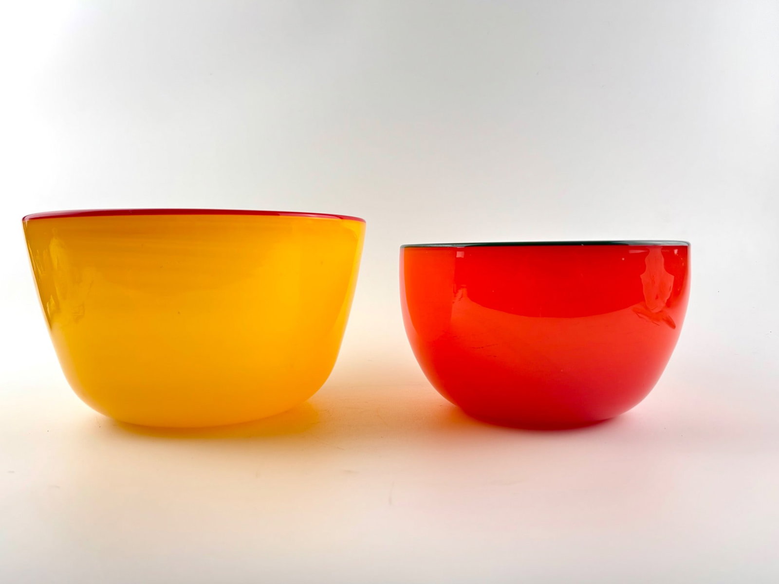 Pete Seacrest Art Glass Bowls with Etched Signature: Art glass bowls designed by Pete Seacrest, one in yellow with a red edge and the other in deep orange with a green edge. Both bowls feature etched signatures on their bases. Minimal visible signs of h