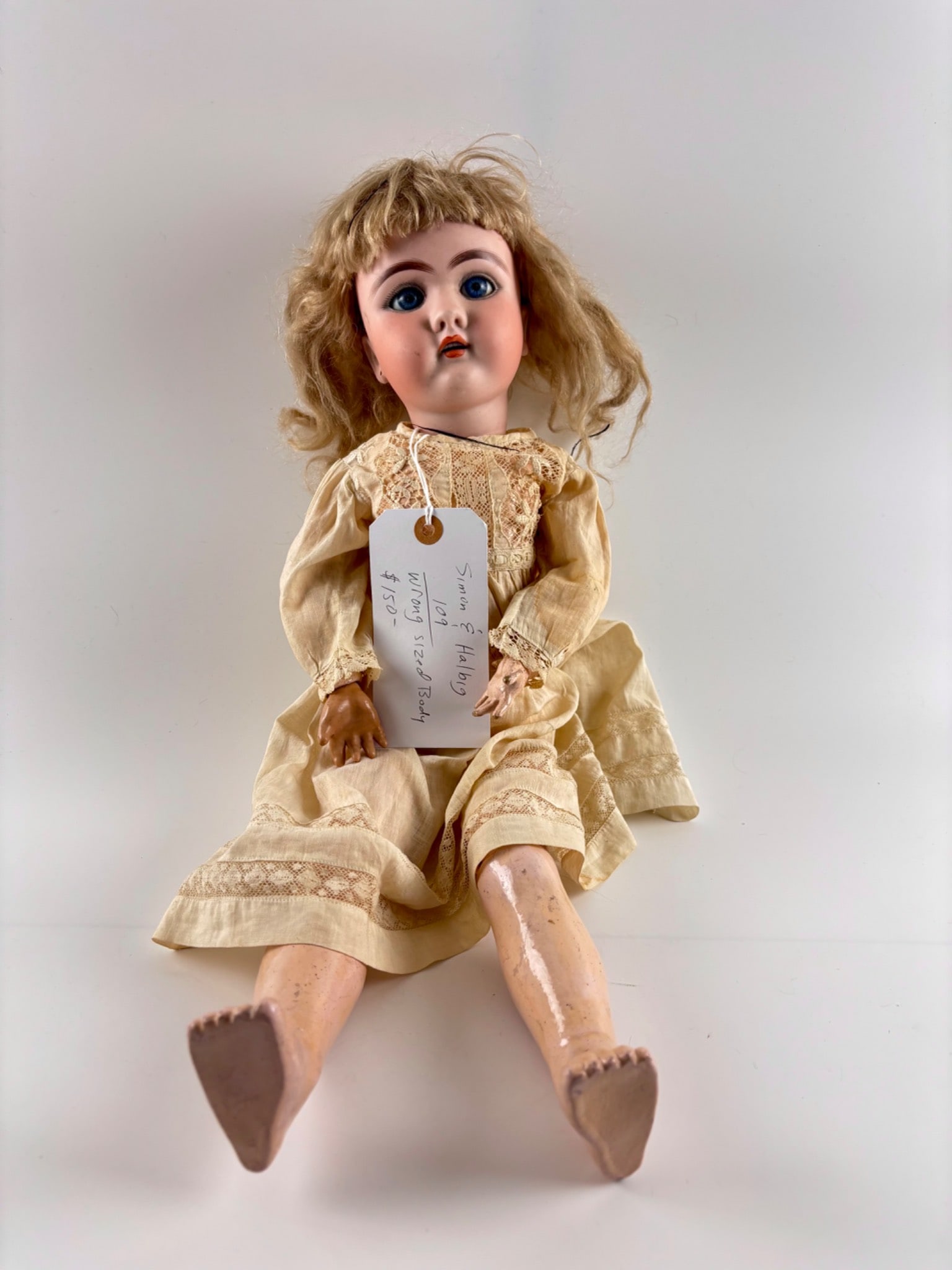 Simon and Halbig Bisque Head Doll 109: Simon and Halbig bisque head doll with a German makers mark on the back of the head. Features sleeping blue glass eyes, painted eyelashes, and open mouth with teeth. Blonde wig over the head. The comp