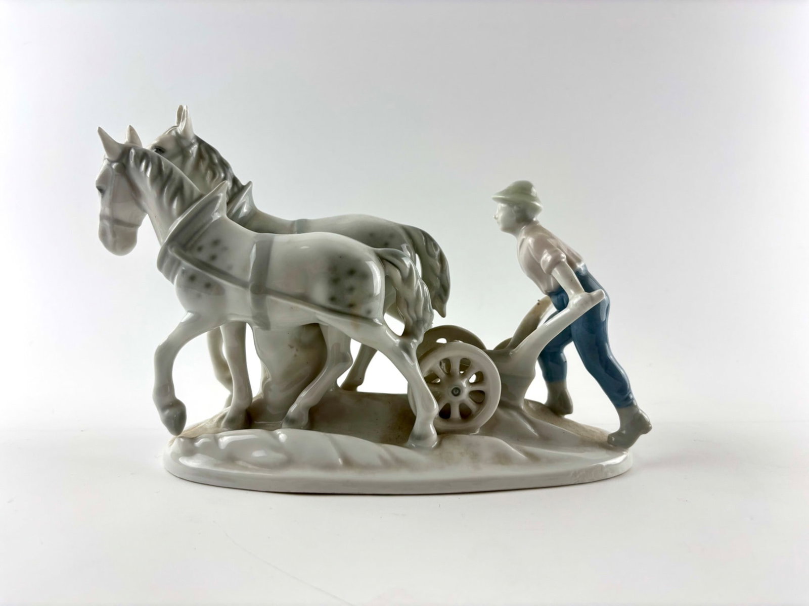 Gerold and Co. Bavaria Porcelain Figurine of Farmer with Horses: Porcelain figurine by Gerold and Co., Bavaria featuring a farmer guiding two horses pulling a plow. The piece displays fine detailing, including the horses’ textured manes and spotted bodies. The fa