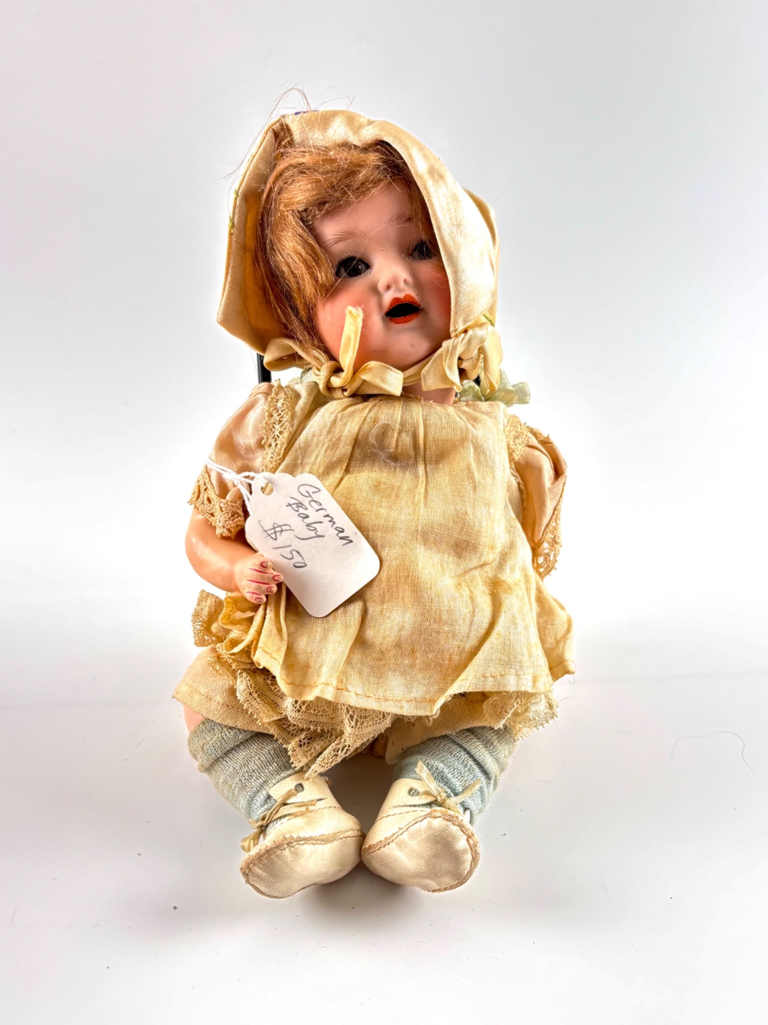 German Bisque Head Open Mouth Baby Doll: German bisque head baby doll featuring sleep eyes, painted features, and a composition body. The doll is dressed in its original cream-colored dress with lace detailing and matching bonnet, as well as
