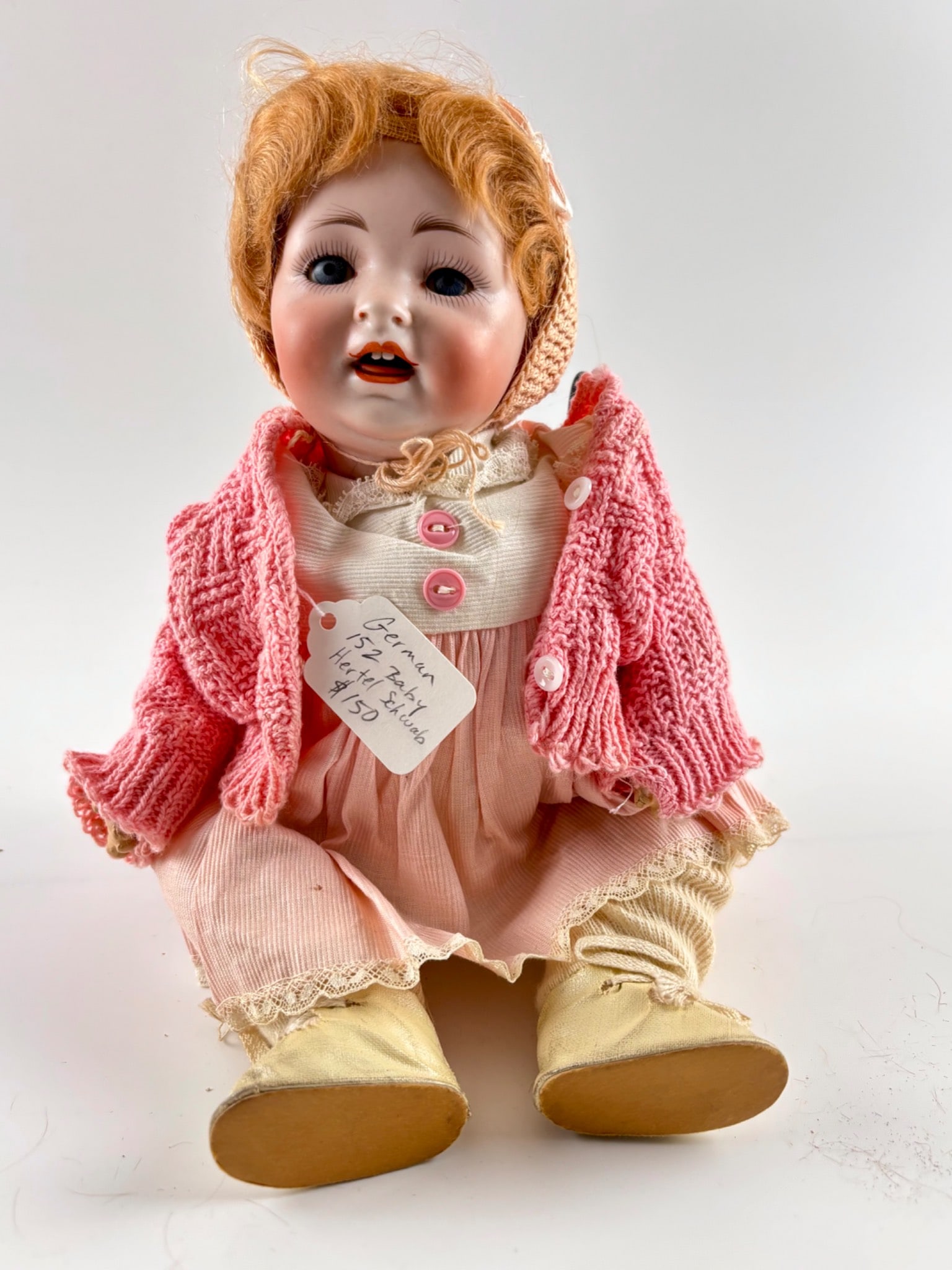Hertel Schwab German Bisque 152 Baby Doll with Sleep Eyes: Hertel Schwab German bisque baby doll, model 152, featuring sleep eyes, open mouth with teeth, and a composition body. The doll is dressed in a pink knit sweater, matching pink dress, lace trim, and c