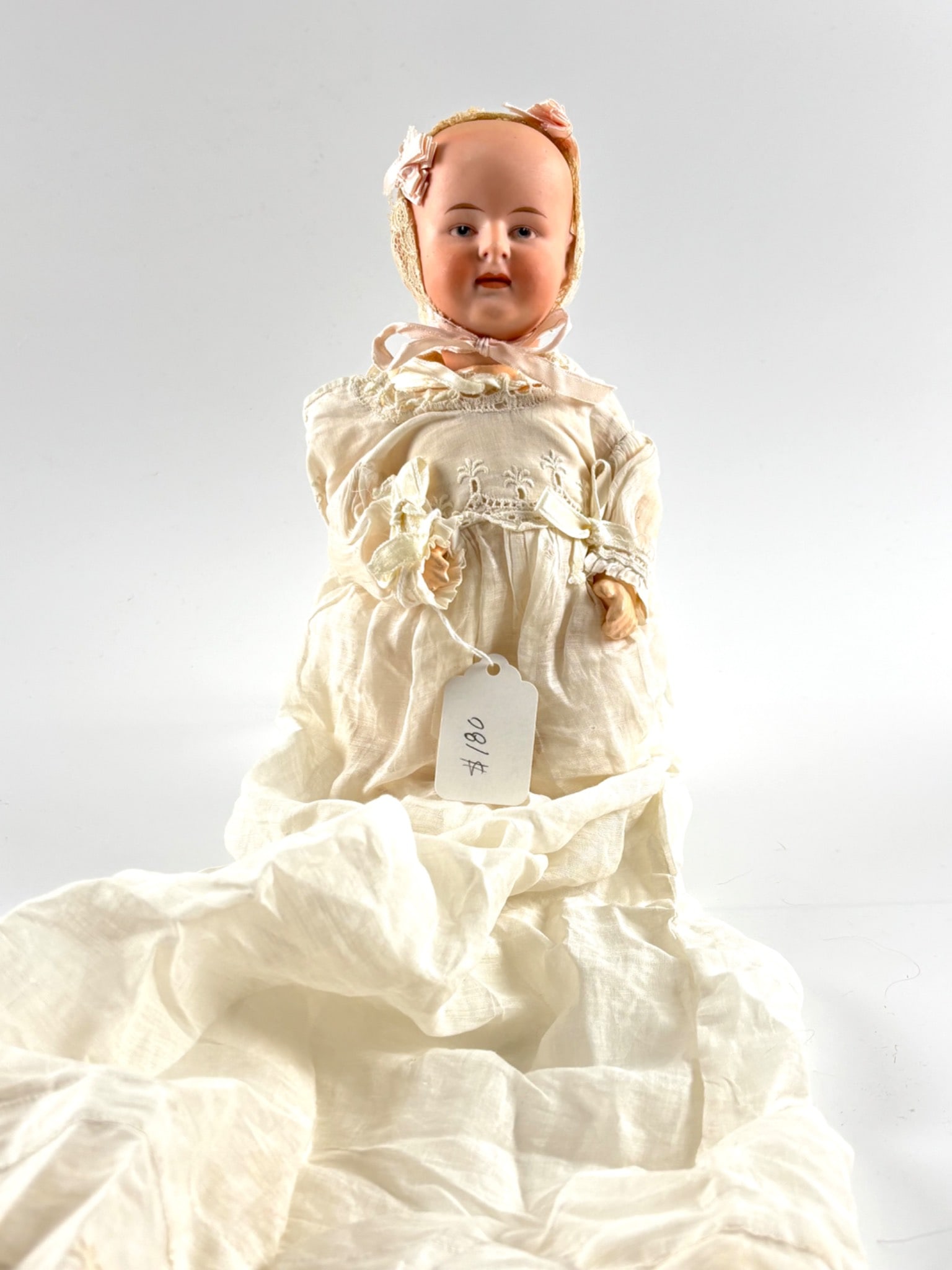 Antique Heubach Baby Doll with Intaglio Eyes: Heubach bisque head baby doll featuring painted intaglio eyes, molded lips, and finely molded facial details. Marked with a handwritten tag indicating Heubach. Dressed in an antique white christening