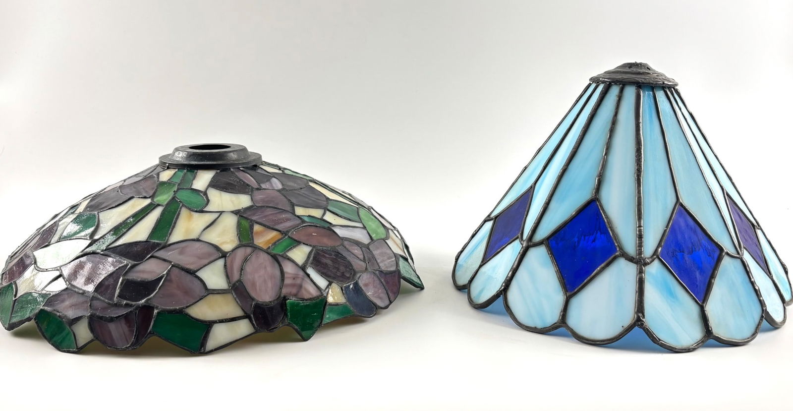 Stained Glass Lamp Shades Featuring Floral and Geometric Designs: Stained glass lamp shades. The first features a dome shape with floral motifs in shades of green, purple, and white, constructed from cut stained glass with lead soldering. The second is a conical sha