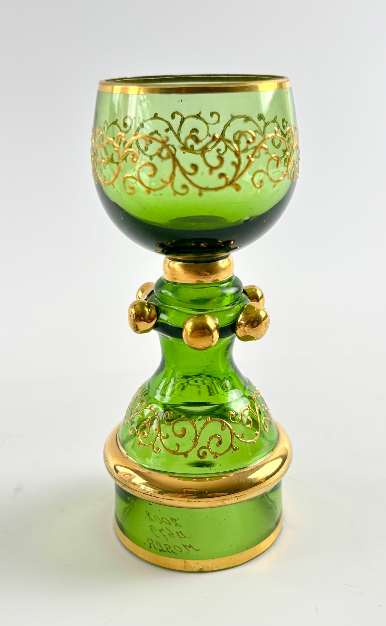 Moser Olive Green Glass Goblet with Applied Prunts: Moser green glass goblet featuring elaborate gilt scrollwork decoration and a band of gilt trim along the rim and base. The stem is adorned with applied gold tone globules and gilt details. Marked ‘