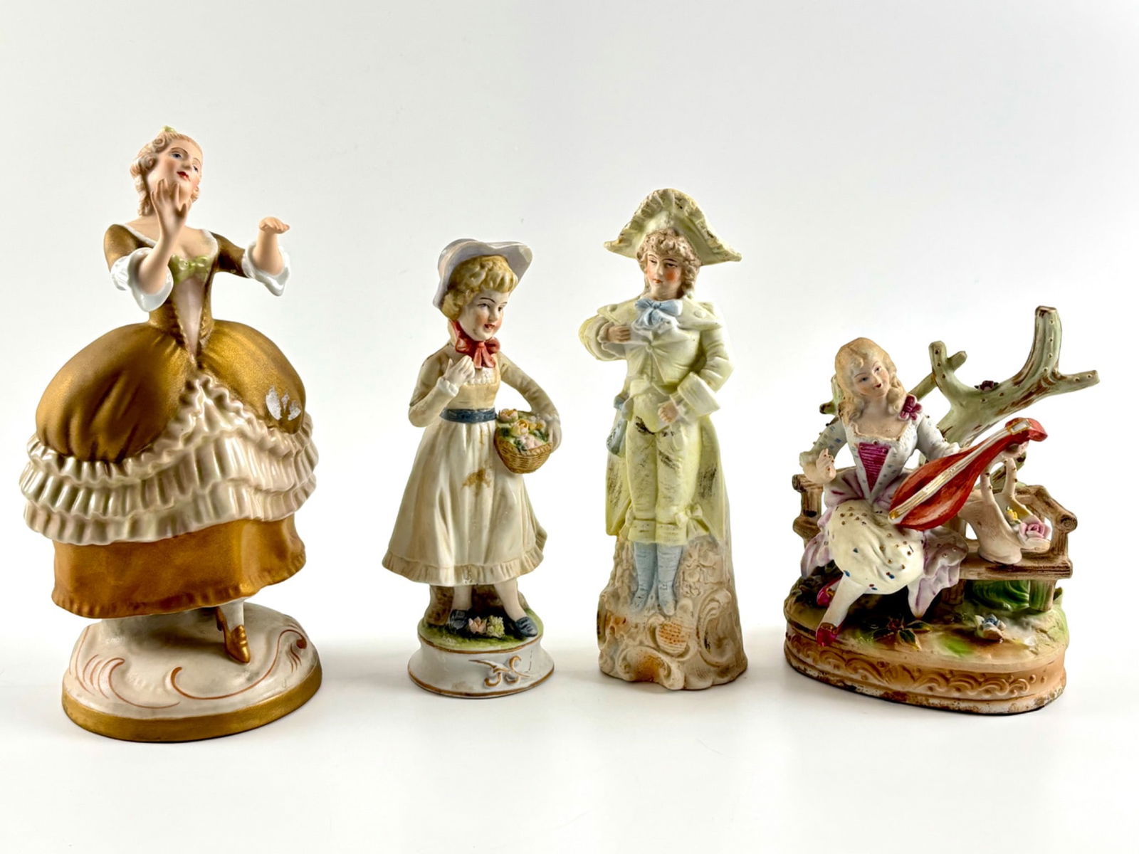 Four Hand Painted Porcelain Figurines with Royal Dux and Markings: Four hand painted porcelain figurines featuring a ballerina, a young girl with a basket, a seated lady playing a stringed instrument, and a gentleman in 18th century attire. The figurines display vibr