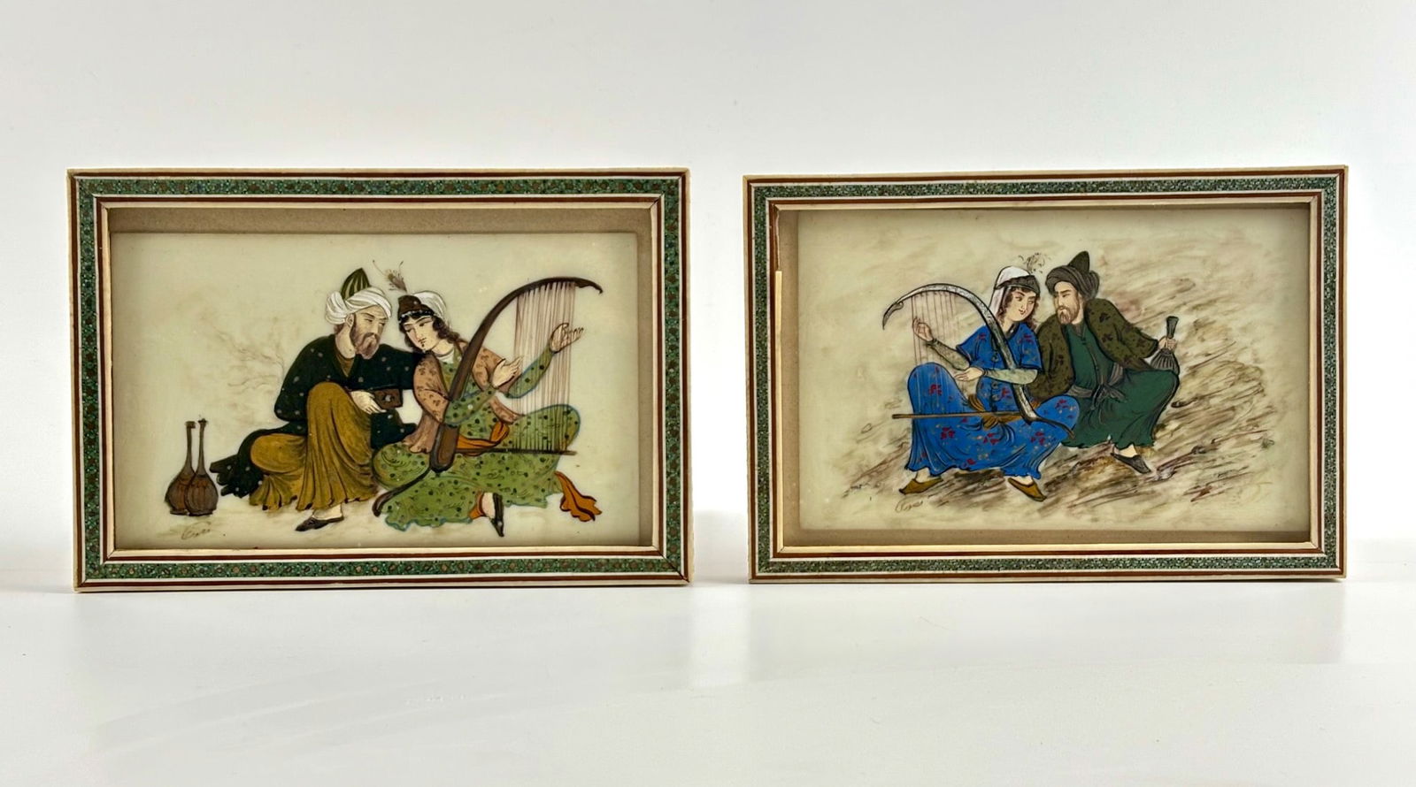 Persian Camel Bone Miniature Paintings in Decorated Frames: Persian miniature paintings on camel bone, depicting traditional scenes featuring seated figures in intricate attire, with musical instruments and detailed expressions. Both pieces are framed in wood