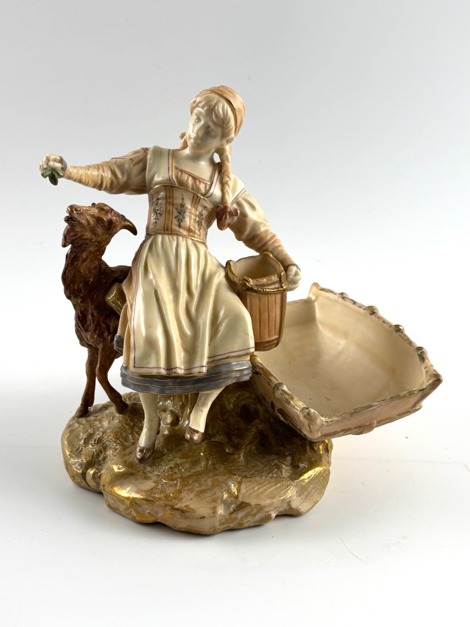 Royal Worcester Figurine of Girl and Goat: Royal Worcester porcelain figurine featuring a young girl holding a small green branch, standing beside a goat and a cart. Detailed polychrome hand painted decoration with gilt accents adds exceptiona