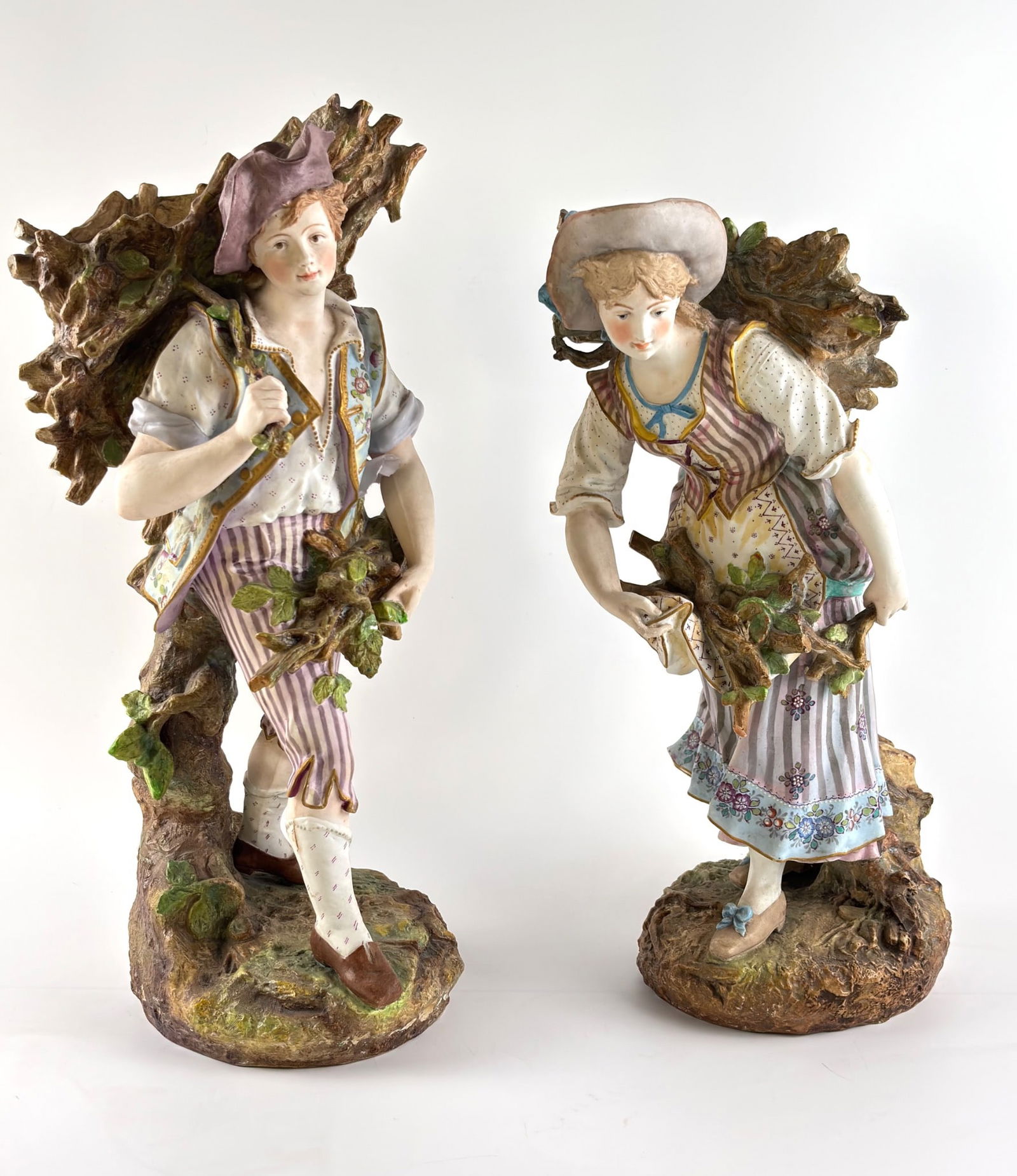 Large Volkstedt and Rudolstadt Porcelain Figurines: Large porcelain figurines from Volkstedt and Rudolstadt. The male figurine depicts a woodcutter with a bundle of branches, wearing a striped vest, purple hat, and striped pants, accented by floral det